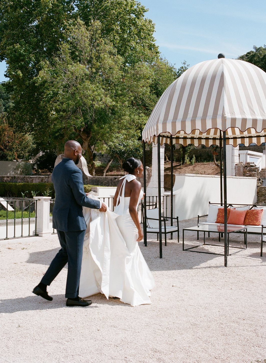 A bride and groom walking past a striped garden pavilion in Lisbon, Portugal